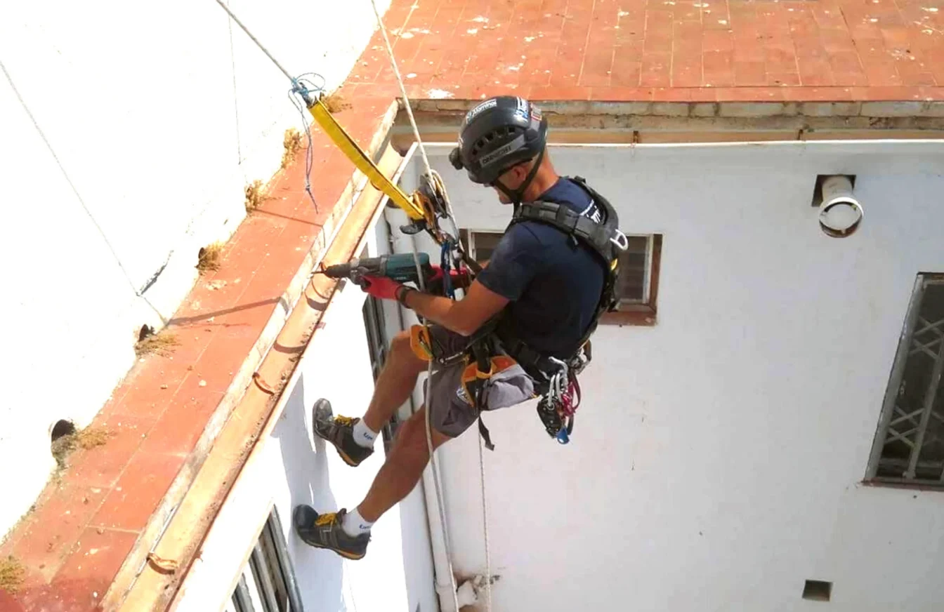 Operario colgado sobre la fachada de un edificio y sujetado por un arnés mientras realiza un trabajo vertical