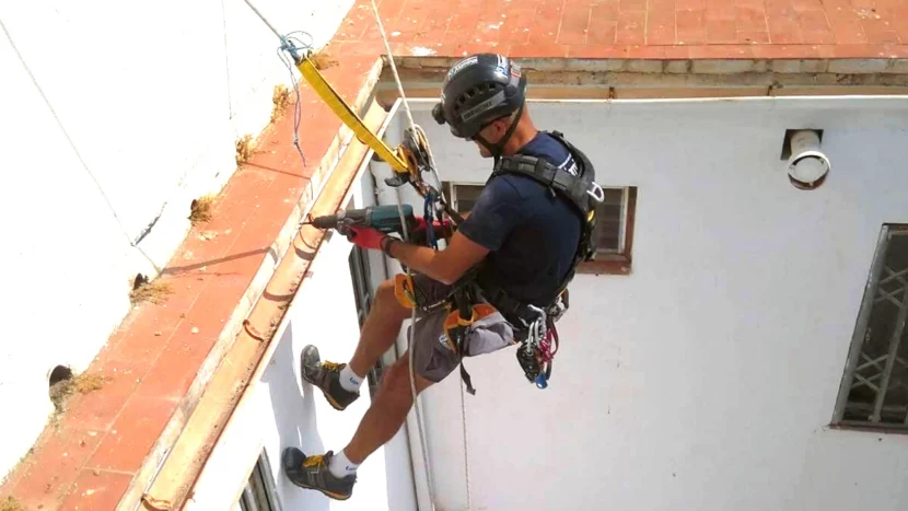 Operario colgado sobre la fachada de un edificio y sujetado por un arnés mientras realiza un trabajo vertical